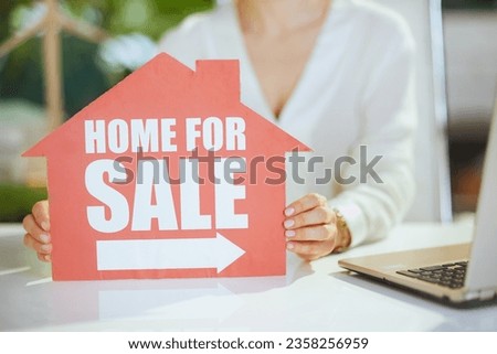 Sustainable real estate business. Closeup on middle aged woman real estate agent in green office in white blouse with home for sale sign.