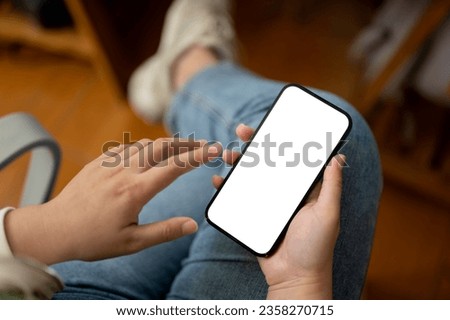 Close-up image of a female in jeans using her smartphone while sitting in a room. Smartphone white screen mockup