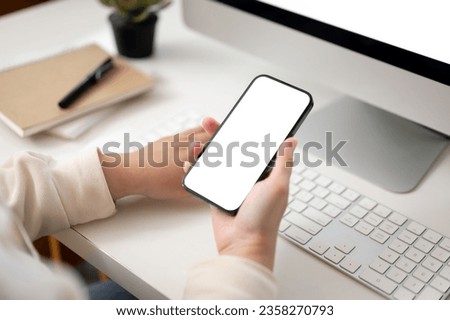 Close-up image of a female office worker using her smartphone while working on her computer at her desk in the office. smartphone white screen mockup Royalty-Free Stock Photo #2358270793