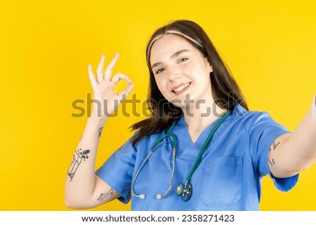Portrait of pretty cheerful Young caucasian doctor woman wearing blue uniform make selfie show okey symbol