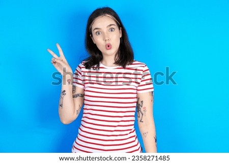 Young caucasian woman wearing striped t-shirt makes peace gesture keeps lips folded shows v sign. Body language concept