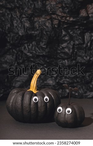 Two black pumpkins with eyes on an black background. Pumpkin monsters, funny Halloween vertical card, copyspace for text