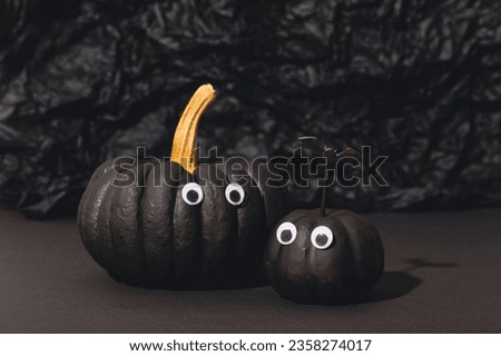 Two black pumpkins with eyes on an black background. Pumpkin monsters, funny Halloween card