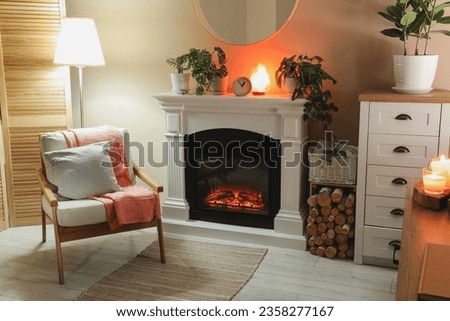 Stylish fireplace near comfortable armchair in cosy living room. Interior design