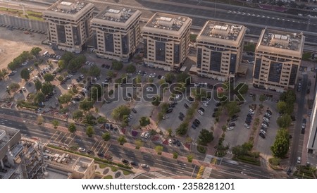 Aerial view of many colorful cars parked on parking lot with lines and markings for parking places at evening timelapse. Green trees around. Financial district in Dubai near sheikh zayed road