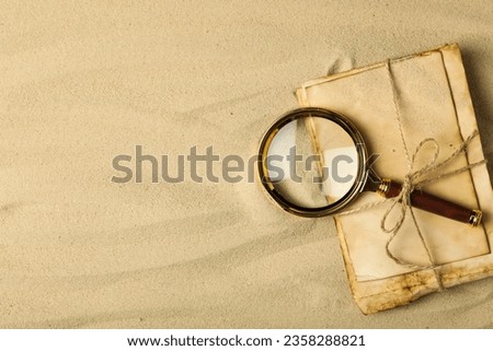 Columbus Day. A magnifying glass with a stack of letters on the sand