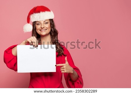 Happy Christmas woman in Santa hat with blank empty paper banner board on colorful pink background, Xmas portrait