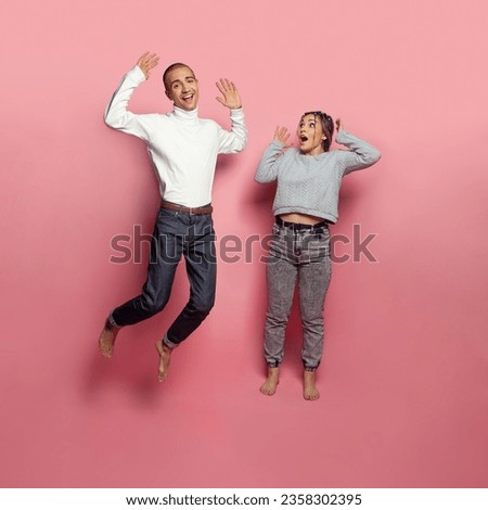 Jumping man and woman having fun on brigtht pink studio wall background