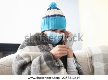 Sick woman in hat under blanket on self isolation holds pills in her hands Royalty-Free Stock Photo #2358313619