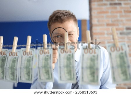 Man looks through magnifying glass at one hundred dollar bills hanging on clothespins. Royalty-Free Stock Photo #2358313693