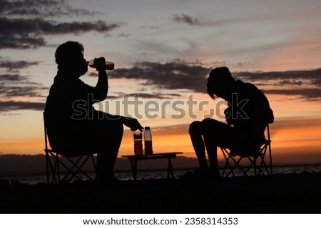 Silhouette of two young men standing by the lake enjoying the sunset. peaceful atmosphere in nature
