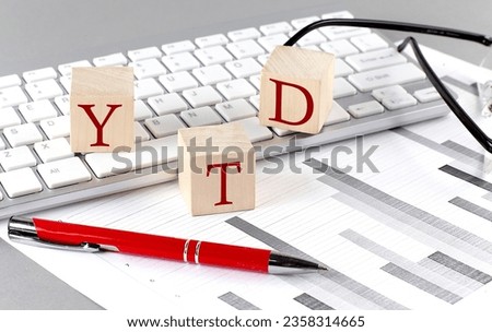YTD written on wooden cube on the keyboard with chart on grey background