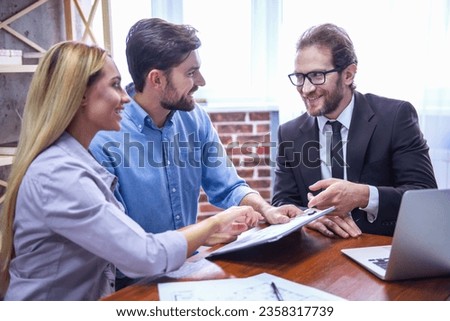 Beautiful couple is examining documents with handsome realtor in suit and smiling
