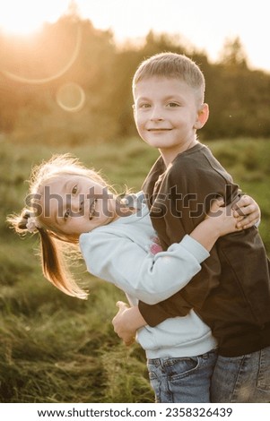 Daughter, son hugging in green grass in field at sunset. Happy children walking spending time together in nature. Concept family holiday outdoors. Kids playing in mountains on autumn day. Closeup