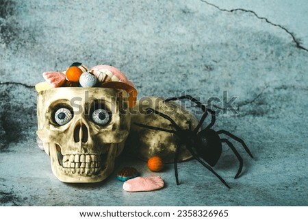 Halloween concept background. Funny halloween skull with chocolate eyes,halloween candies and spider with space for text over grunge background. Halloween party decoration concept