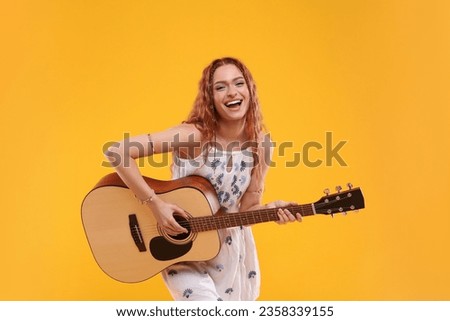Beautiful young hippie woman playing guitar on orange background Royalty-Free Stock Photo #2358339155