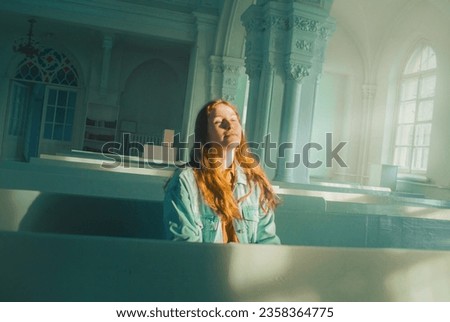 A portrait of a ginger young woman sitting in a bright church. The light streaming in through the windows illuminates her serene expression. Faith, spirituality, and inner peace.