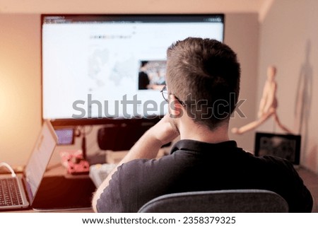 A young geek man engaged in uploading the photos onto the stock website. Stock photographer freelancing at home.