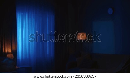 Shot of a flat, house, apartment in the night. Neon blue lights are seen through the window. Late night, muffled light, after midnight.
