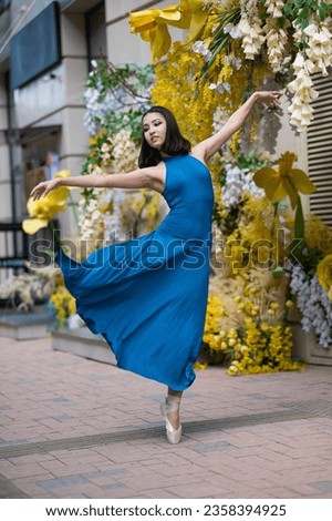 Beautiful Asian ballerina posing against the backdrop of a building decorated with flowers. 
