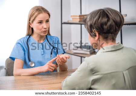Physician in blue uniform with stethoscope telling about advantages of taking medication, giving advice to senior woman at appointment in clinic. Doctor consulting patient about treatment Royalty-Free Stock Photo #2358402145