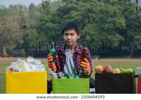 Asian boy in plaid shirt sitting on playground of school with various boxes of separated garbabes or trashes inside, concept for eco friends and global warming campaign, soft and selective focus.