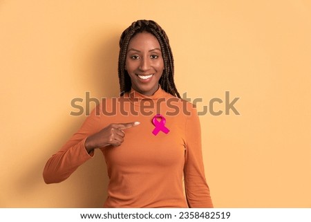 happy black young woman showing pink ribbon in studio shot. breast cancer, awareness concept. Royalty-Free Stock Photo #2358482519