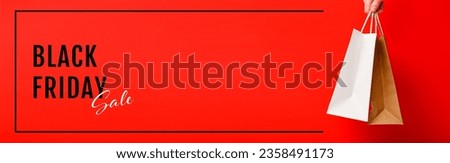 Black Friday sale banner. Female hand holding two shopping bags on red background Royalty-Free Stock Photo #2358491173