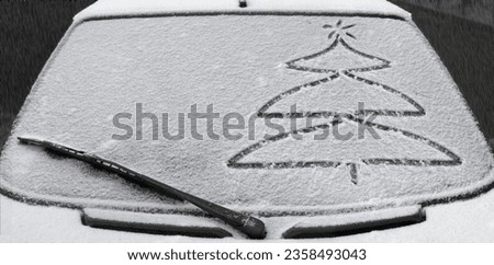 Drawing of a Christmas tree on a snow-covered glass of a car