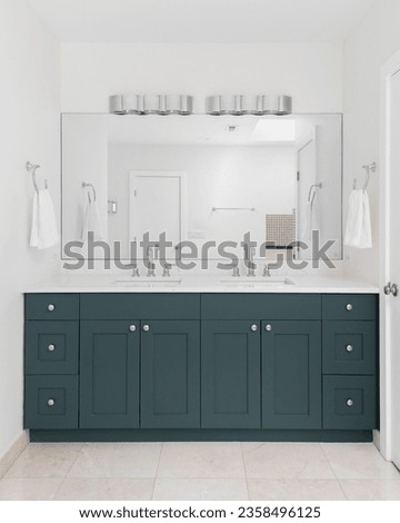 A bathroom with a blue green vanity cabinet, white marble countertop, and stone tile floor. Royalty-Free Stock Photo #2358496125