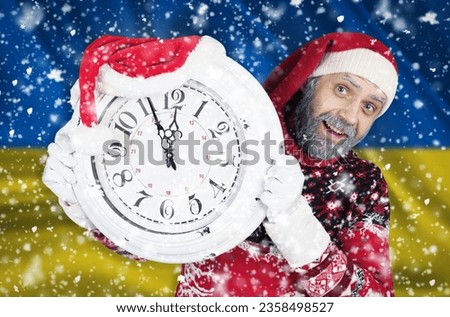 Santa Claus holds a clock in his hands, on which 5 minutes are left until the new year, Christmas, against the background of the flag of Ukraine. New year and christmas concept.