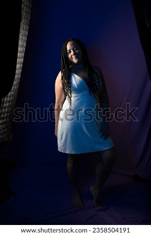Studio portrait of pretty woman with braided hair in white dress posing for photo, standing. Isolated on dark blue colored background. Positive person.