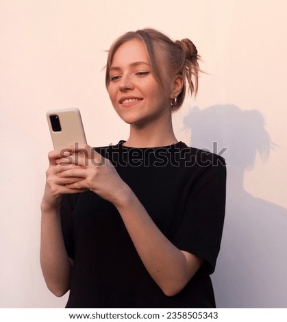 beautiful blond girl in black t-shirt holds a phone smiling and typing message