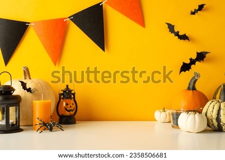 Spookify your table for Halloween. Side view image of a tabletop featuring themed decor, pumpkins, luminous jack-o'-lantern lamp, bats, spiders, candles, and festive flag garland on a yellow wall