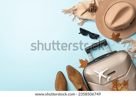 Begin your autumn journey in style. Top view image showcasing gray suitcase, plush cashmere scarf, trendy sunglasses, boots and felt hat on light blue backdrop, ready for your text or advertising Royalty-Free Stock Photo #2358506749
