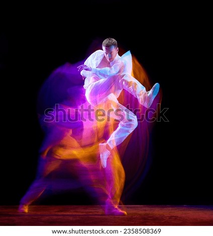 Burst of energy. Young stylish guy in motion, jumping against black studio background in neon with mixed lights effect. Concept of movements, art, dance and sport, fashion, youth, ad