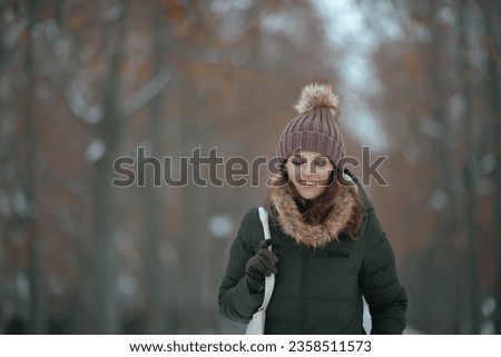happy modern middle aged woman in green coat and brown hat outdoors in the city park in winter with beanie hat. Royalty-Free Stock Photo #2358511573