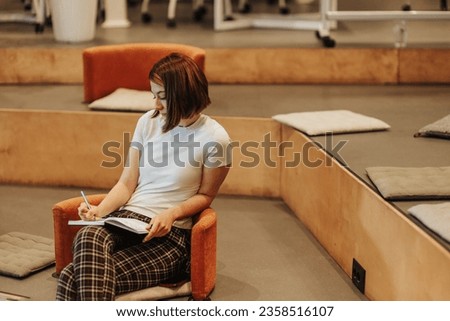 Stunning, short haired woman writing information down in a notebook during seminar at modern comfy working area