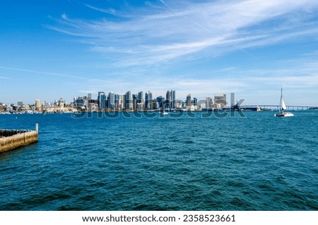 Wide view of San Diego skyline over the water of San Diego Bay. Coronado bridge at right of picture. Taken from tip of Harbor Island. Deep blue water, and bright blue sky with wispy white clouds.