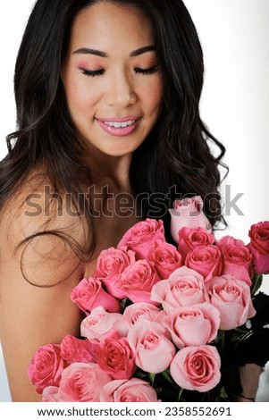Asian woman holding flowers against chest for breast cancer awareness