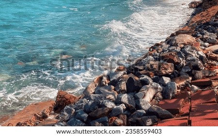 a photography of a beach with a red walkway and a blue ocean, breakwater along the shore of a beach with a red walkway.