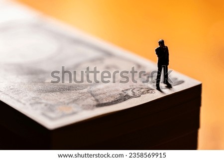 Miniature Businessman Standing on a Pile of Money Bills Royalty-Free Stock Photo #2358569915