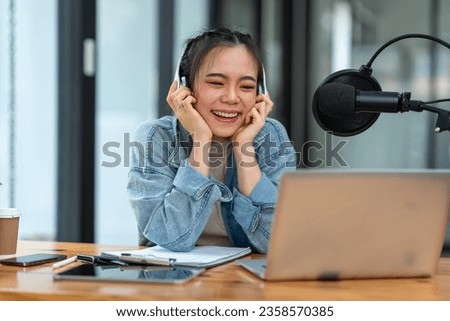 Young Asian businesswoman in headphones talking through microphone in studio, podcast, call center, customer service talking in video conference on laptop computer, tablet or meeting virtual office.