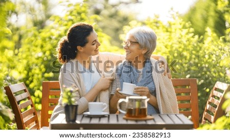 Happy young woman and her mother drinking tea in summer morning. Family sitting in the garden with cups and enjoying the conversation. Royalty-Free Stock Photo #2358582913