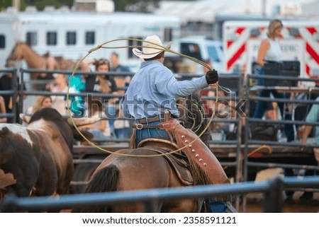A cowboy riding a horse and trying to rope a bull during a rodeo. Royalty-Free Stock Photo #2358591121
