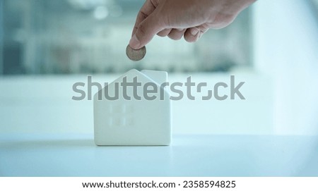 Closeup of hand putting coin in house piggy bank.                               