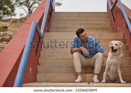 Young Hispanic man, sitting on stairs next to his dog while talking with him in a loving and tender attitude. Concept, dogs, pets, animals, friends. Royalty-Free Stock Photo #2358603899