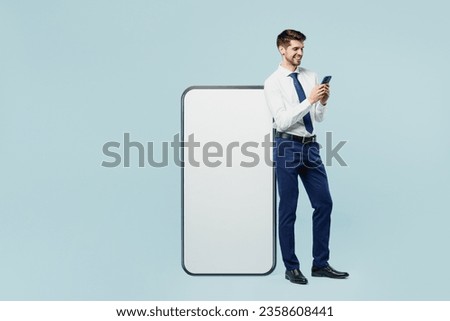 Full body young employee IT business man corporate lawyer in classic formal shirt tie work in office big huge blank screen mobile cell phone with area use smartphone isolated on plain blue background