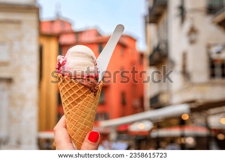Woman s hand holding artisanal chocolate and amarena gelato in a cone, view of traditional colorful houses in the Old Town of Nice, South of France Royalty-Free Stock Photo #2358615723