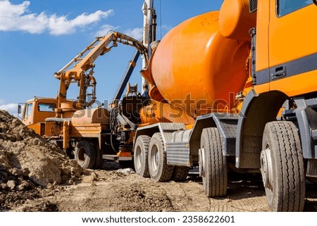 Mixer truck is in process of transshipment at building site. Pouring fresh concrete over ramp to truck with pump machine. Royalty-Free Stock Photo #2358622601